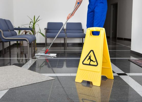 Sinihousuinen ihminen moppaa lattiaa, edessä varoitusmerkki
